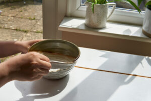 two hands fixing a broken kintsugi pottery bowl