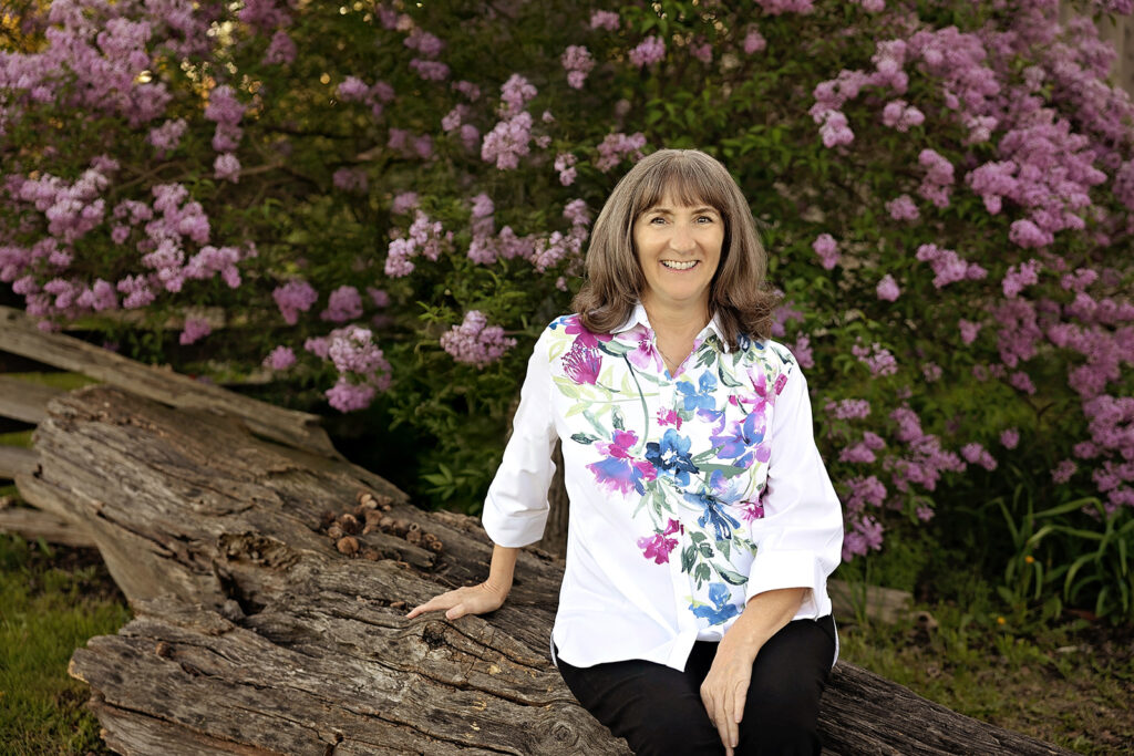 Terry sitting in front of bush with pink flowers.